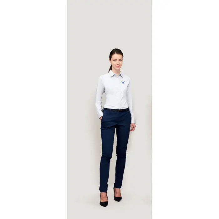 O femeie poartă o cămașă albă EDEN STRETCH pentru femei cu mâneci lungi și logo brodat la piept