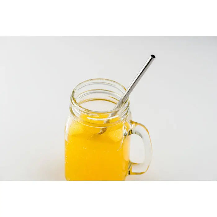 Un pai din oțel inoxidabil cu perie în punga sa, într-un borcan mason cu lichid portocaliu vibrant
