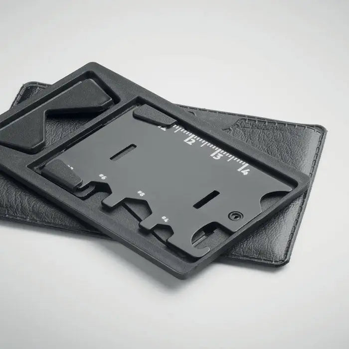 Suport pentru telefon de buzunar negru cu mai multe instrumente si rigla, asezat pe portofel din piele neagra