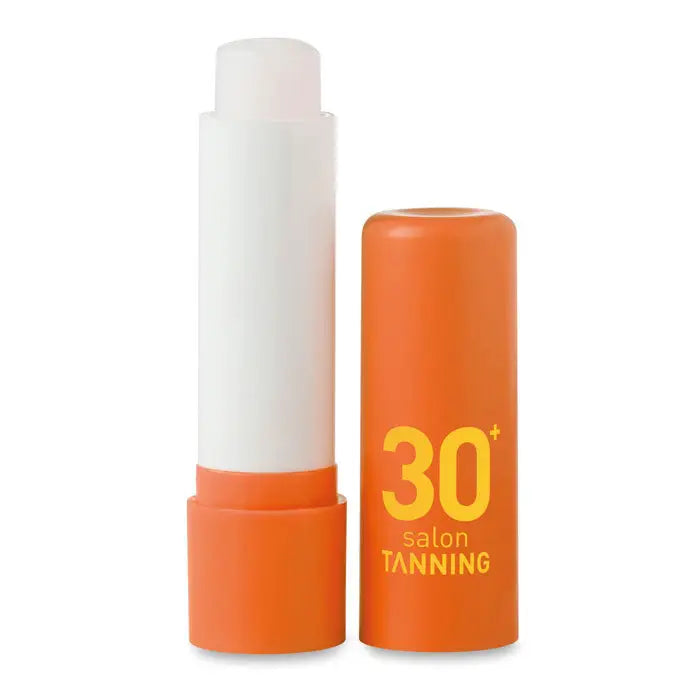 Balsam de buze ambalaj portocaliu cilindric cu text galben 30 plus salon tanning și stick alb de protecție solară