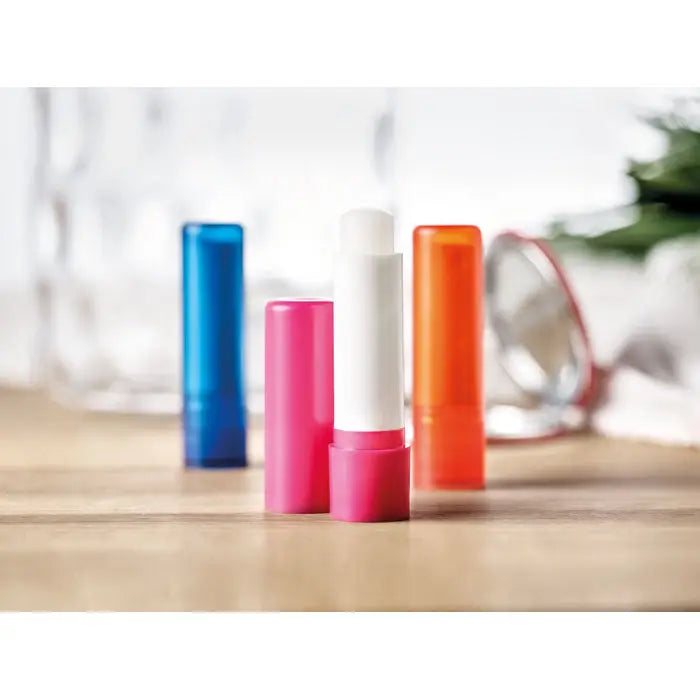 Un tub vibrant de balsam de buze roz cu capac alb, poziționat vertical printre alți balsamuri colorate