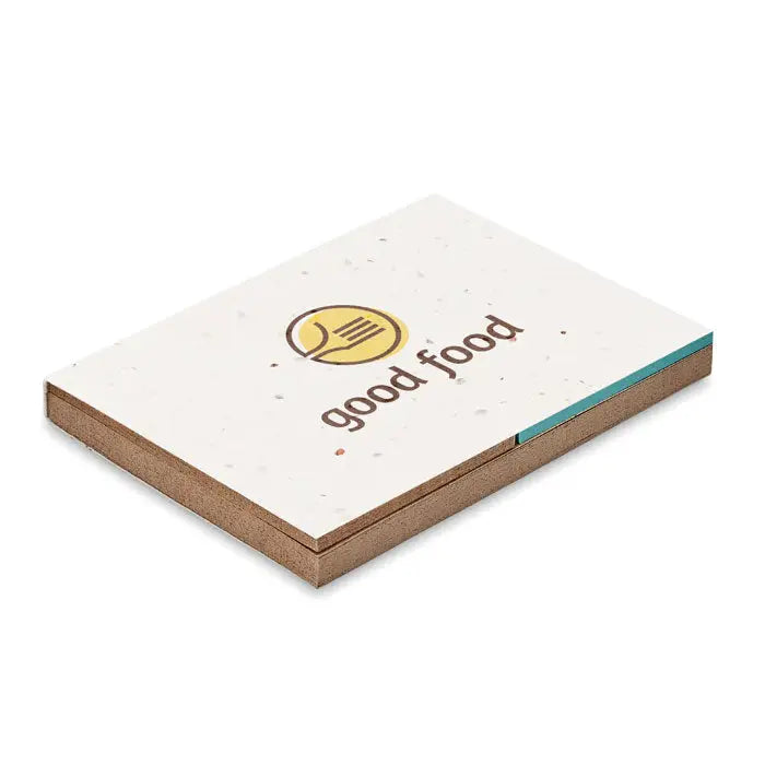 Bloc de note alb cu pete, logo galben si text maro good food, realizat din hartie cu iarba si seminte