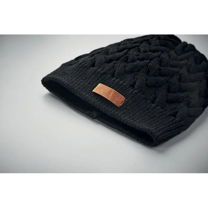 Bonita din tricot cablu rpET este o caciula neagra cu snur texturat si patch maro din piele pe margine pliata