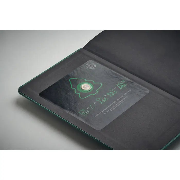Caiet a5 cu pagini reciclate coperta verde inchis din piele cu fereastra transparenta ce arata moneda metalica cu design copac