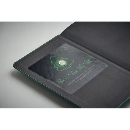 Caiet a5 cu pagini reciclate coperta verde inchis din piele cu fereastra transparenta ce arata moneda metalica cu design copac