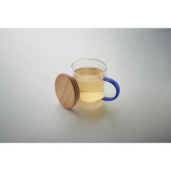Cană din borosilicat cu perete dublu, mâner albastru și capac din lemn natural, umplută cu ceai auriu