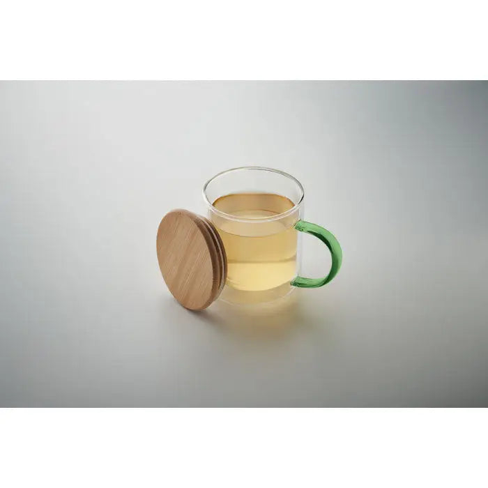 Cana din borosilicat cu perete dublu, mâner verde vibrant și capac din lemn natural, plină cu ceai auriu