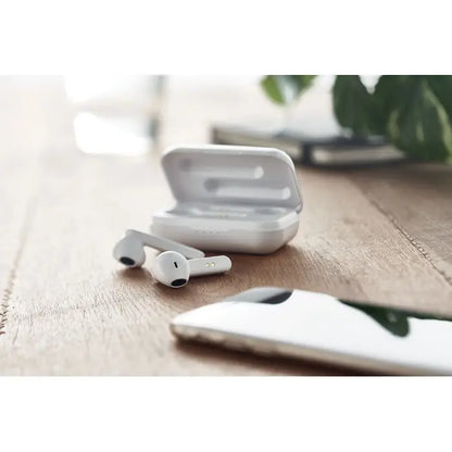 Casti tws albe wireless cu design minimalist si carcasa de incarcare asezate pe o suprafata de lemn