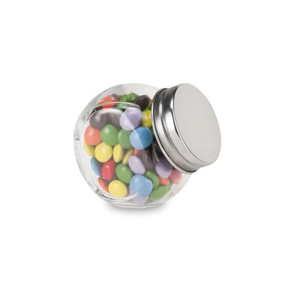 Borcan de sticlă transparent cu capac metalic argintiu umplut cu bomboane colorate ciocolata in suport de sticla