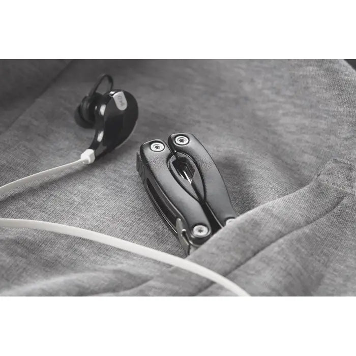 Cutit multifunctional pliabil negru cu accente metalice lângă căști negre pe țesătură gri