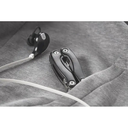 Cutit multifunctional pliabil negru cu accente metalice lângă căști negre pe țesătură gri