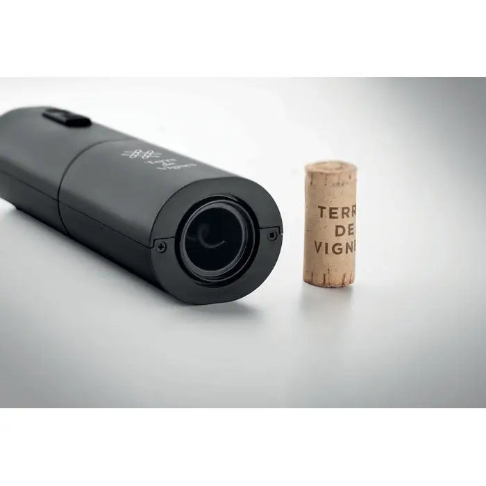 Deschidetor de sticle de vin electric negru cilindric cu grip texturat si marcaje gravate langa un dop natural