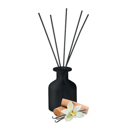Difuzor de trestie de parfum de casa din sticla mata neagra cu bete subtiri negre si pastai de vanilie langa el