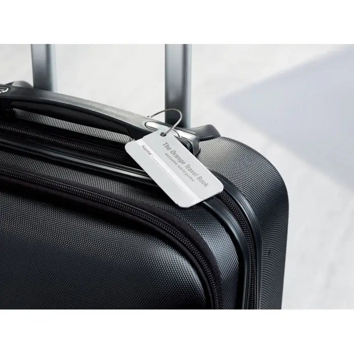 Eticheta de bagaje din aluminiu pe o valiză neagră texturată cu etichetă argintie the orange travel book