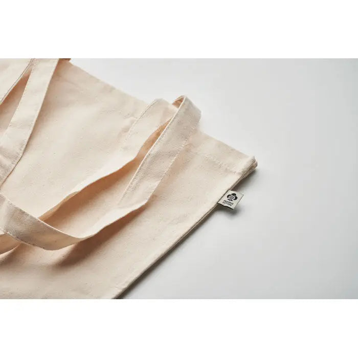 Geanta de cumparaturi din bumbac organic beige cu manere robuste si eticheta mica cu brand