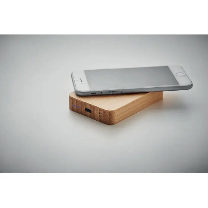 Iphone argintiu așezat pe un încărcător magnetic wireless 10w din bambus cu port usb-c vizibil