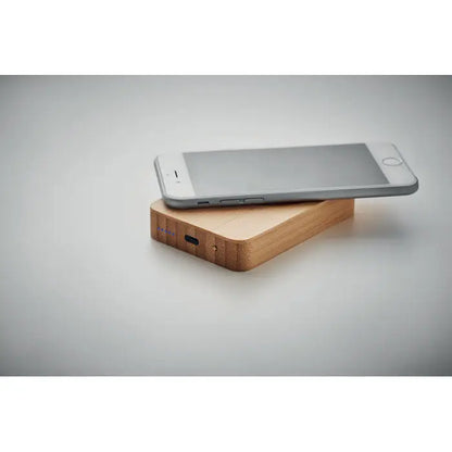 Iphone argintiu așezat pe un încărcător magnetic wireless 10w din bambus cu port usb-c vizibil