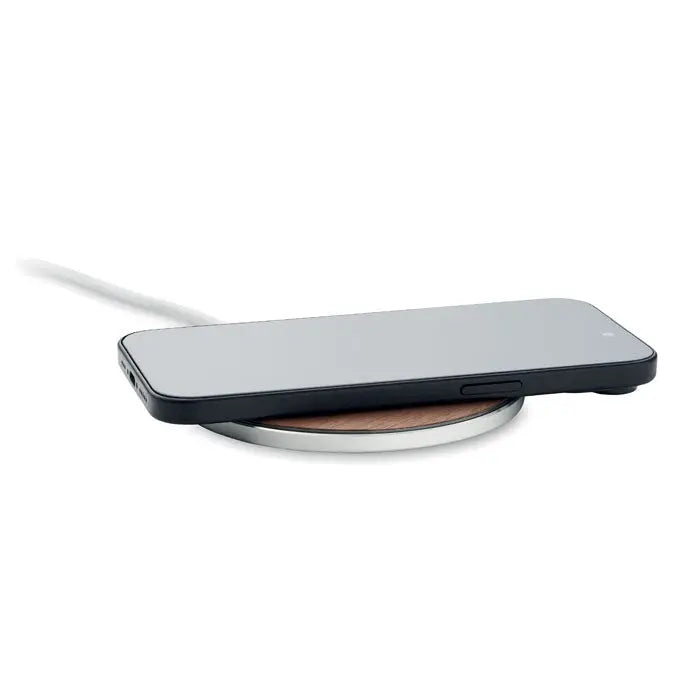 Un smartphone negru elegant se încarcă wireless pe un încărcător circular 15w cu centru din lemn și margine metalică argintie