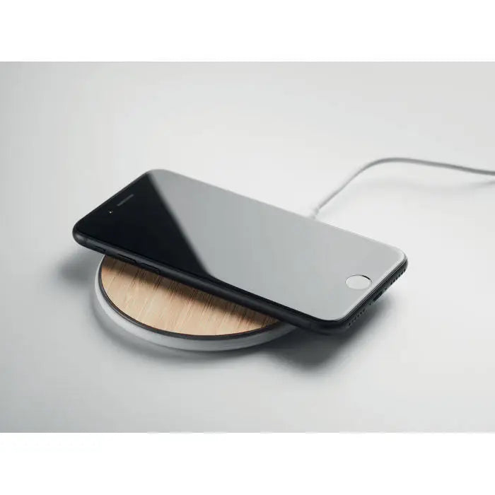 Smartphone negru așezat pe un încărcător wireless Bamboo 10W rotund din lemn cu margine albă