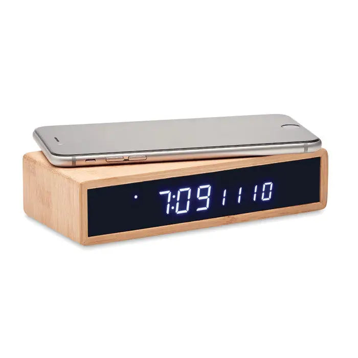 Un ceas digital din lemn cu afisaj led albastru si incarcare wireless 5w din bambus cu un smartphone argintiu deasupra