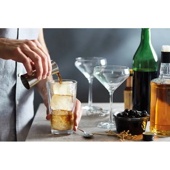 Un shaker de cocktail metalic lucios din otel inoxidabil toarna un lichid inchis intr-un pahar