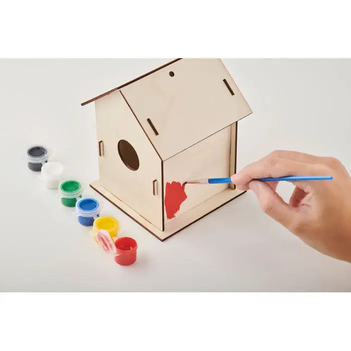 Kit bricolaj pentru casa pentru pasari din lemn cu gaură circulară fiind vopsit roșu pe lateral cu pensulă albastră
