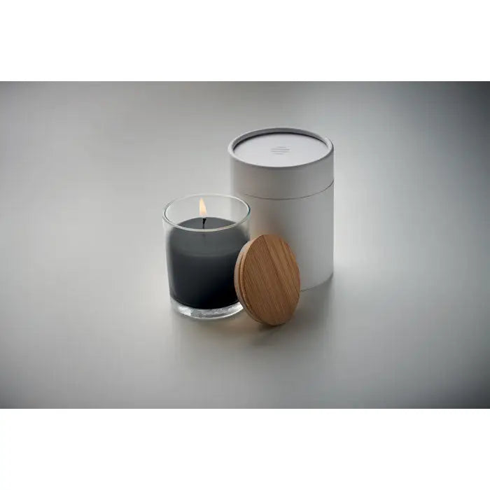 Lumanare cu parfum de vanilie neagra in borcan de sticla transparenta cu capac de lemn langa ambalaj cilindric alb