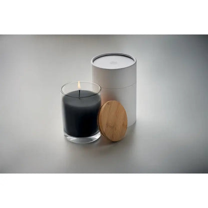 Lumanare cu parfum de vanilie în borcan transparent cu fitil aprins, ambalaj cilindric alb și capac din bambus