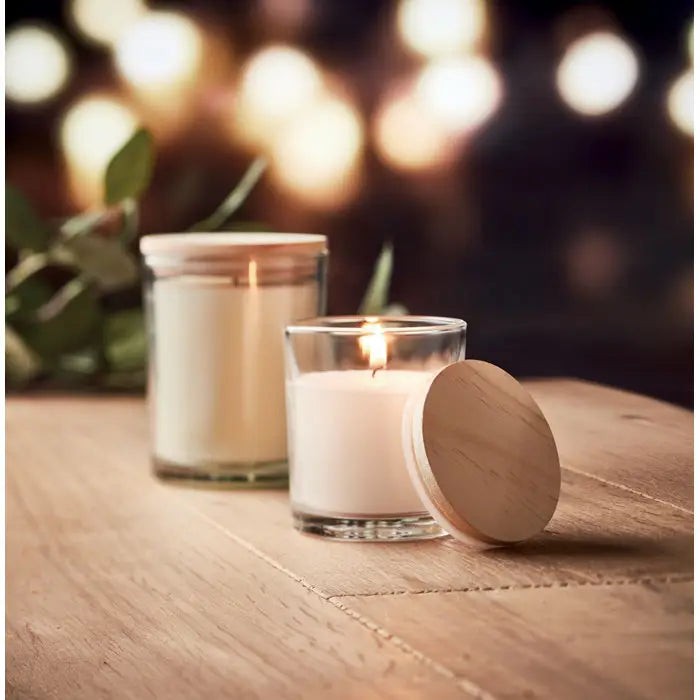 Lumanare cu parfum de vanilie alba in borcan de sticla transparent cu capac din lemn usor aprinsa si lumineaza cald