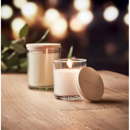 Lumanare cu parfum de vanilie alba in borcan de sticla transparent cu capac din lemn usor aprinsa si lumineaza cald