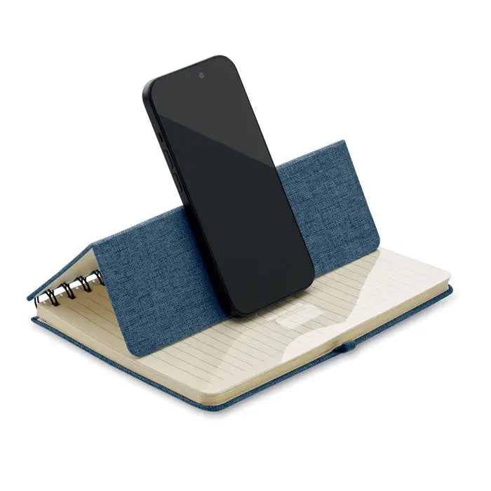 Notebook a5 albastru texturat din denim cu suport integrat pentru telefon tinand un smartphone negru