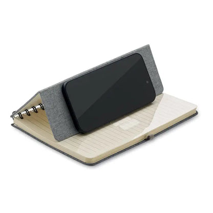 Notebook a5 gri texturat cu suport integrat pentru telefon tinand un smartphone negru