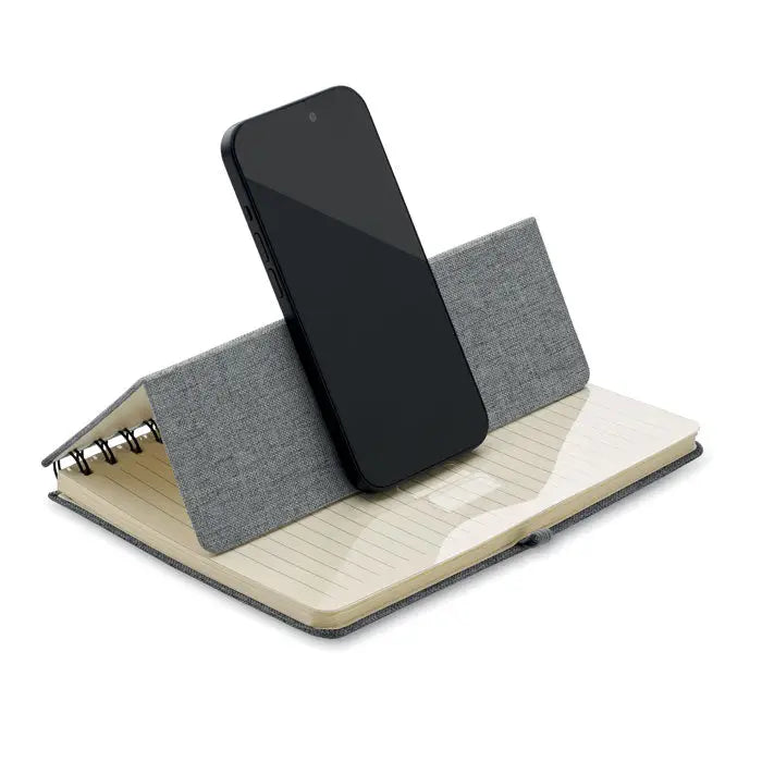 Notebook a5 gri texturat cu suport integrat pentru telefon ținând un smartphone negru