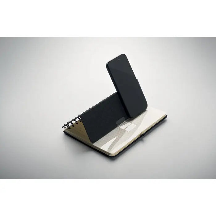 Notebook a5 cu suport pentru telefon negru sprijinit pe un suport spiralat din metal pentru birou