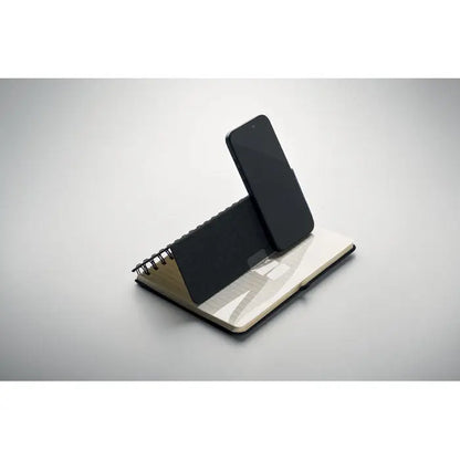 Notebook a5 cu suport pentru telefon negru sprijinit pe un suport spiralat din metal pentru birou