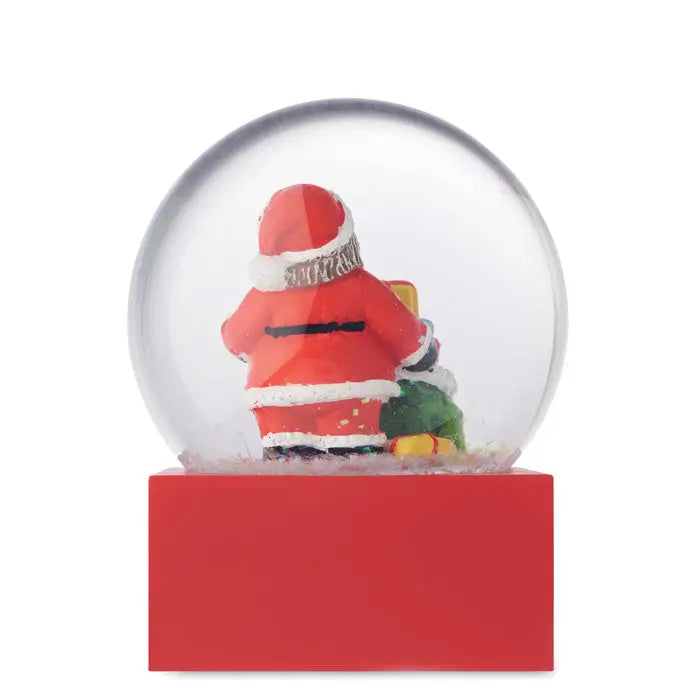 Ornament de sticla cu bile de zapada rosu cu glob de zapada si figura mos craciun in costum rosu langa brad verde