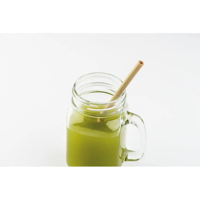 Un borcan mason transparent cu mâner umplut cu lichid verde și o paie de bambus cu perie într-o pungă naturală