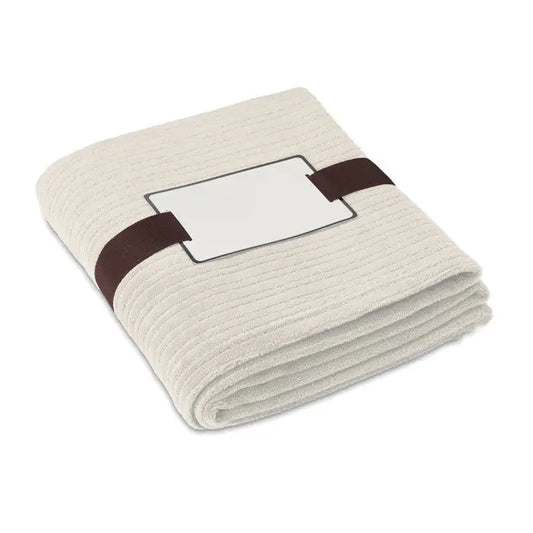Pătură de lână beige cu model riplat, bandă maro închis și etichetă albă, 240 gr/m2, ideală pentru confort acasă