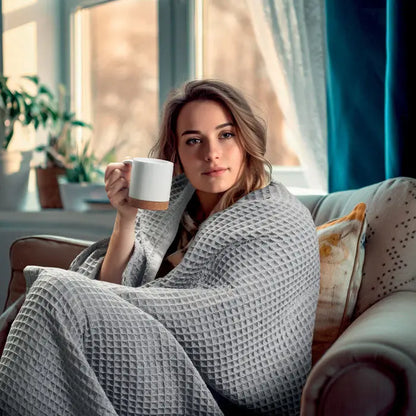 Patura de vafe de bumbac gri 350 gr/m² texturata in fiecare parte invelita in jurul unei femei pe canapea