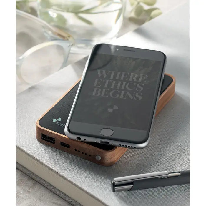 Iphone argintiu pe pad de incarcare wireless din lemn cu porturi usb power bank wireless de 4000 mah minimalista