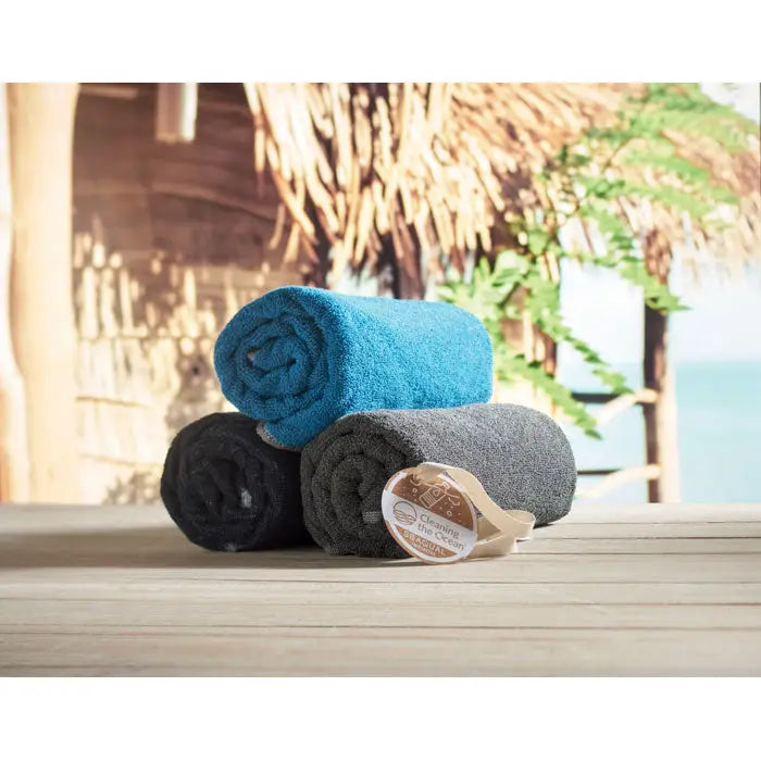 Prosop seaqual 70x140cm din material reciclabil albastru, negru si gri, rulat si stivuit pe o suprafata de lemn