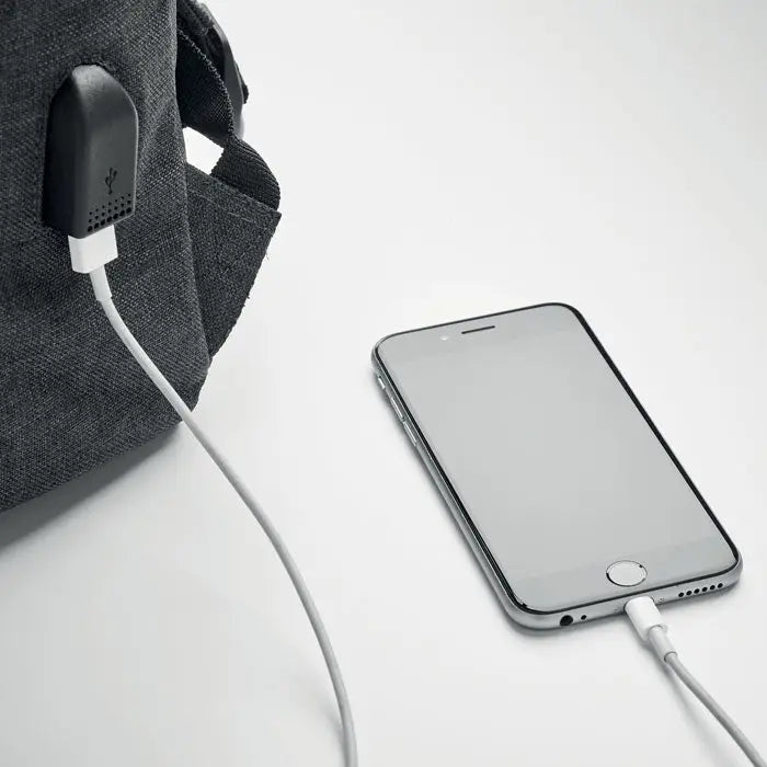 Un iphone 6s plus argintiu elegant conectat la cablu de incarcare pe o suprafata alba langa un rucsac din poliester 600D