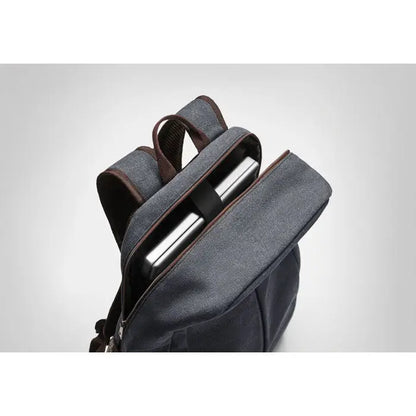 Rucsac pentru laptop din panza gri închis cu garnituri din piele maro și laptop argintiu în interior