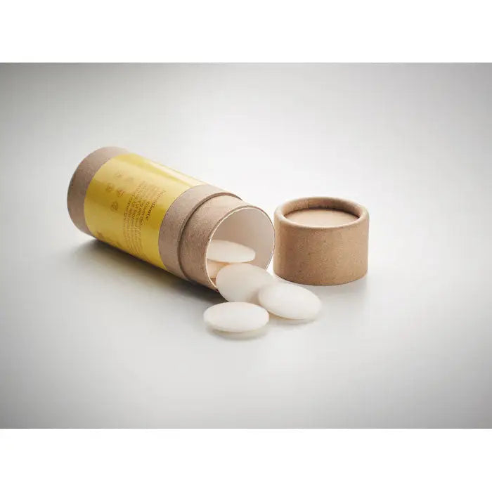 Tablete albe rotunde cu margini netede care ies dintr-un tub cilindric de carton cu eticheta galbena pentru sampon vegan unisex