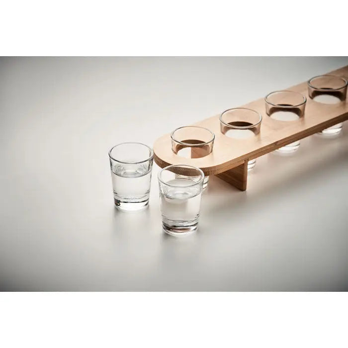 Set de 6 pahare de shot din sticla clara aranjate pe un suport de lemn deschis la culoare