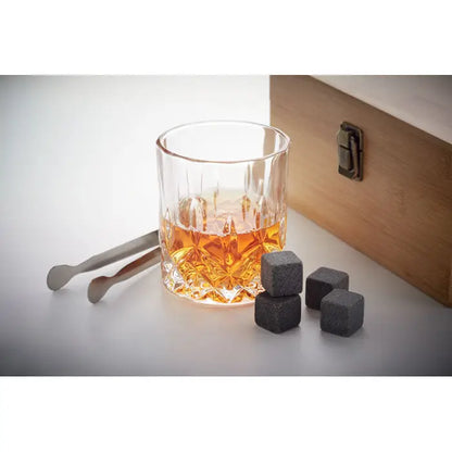 Set de whisky în cutie de bambus cu pahar clar și fețat umplut cu lichid ambr și cuburi din piatră gri închis