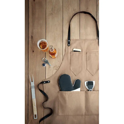 Sort din piele tan canvas apron with black leather straps and multiple pockets holding barbecue tools