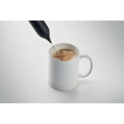 Spumator electric pentru lapte negru din plastic în utilizare deasupra unei cești ceramice albe