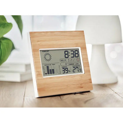 Statie meteo fata din bambus cu rama patrata din lemn natural si afisaj alb ce arata ora temperatura umiditatea si prognoza