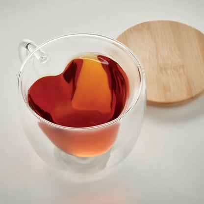 Sticla borosilicata cu perete dublu mug transparent cu ceai ambrat si suprafata lichida in forma de inima cu capac lemn deschis